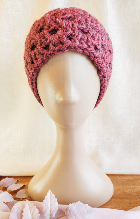 Pink knitted headband on a mannequin head with seashells in the foreground