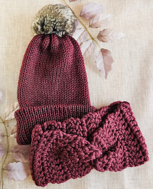 Knitted maroon hat and scarf set with fur pom-pom on a light background