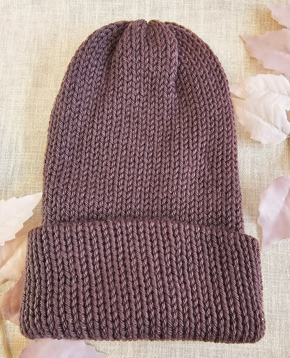 Brown knitted beanie on a textured beige background with pink flowers.