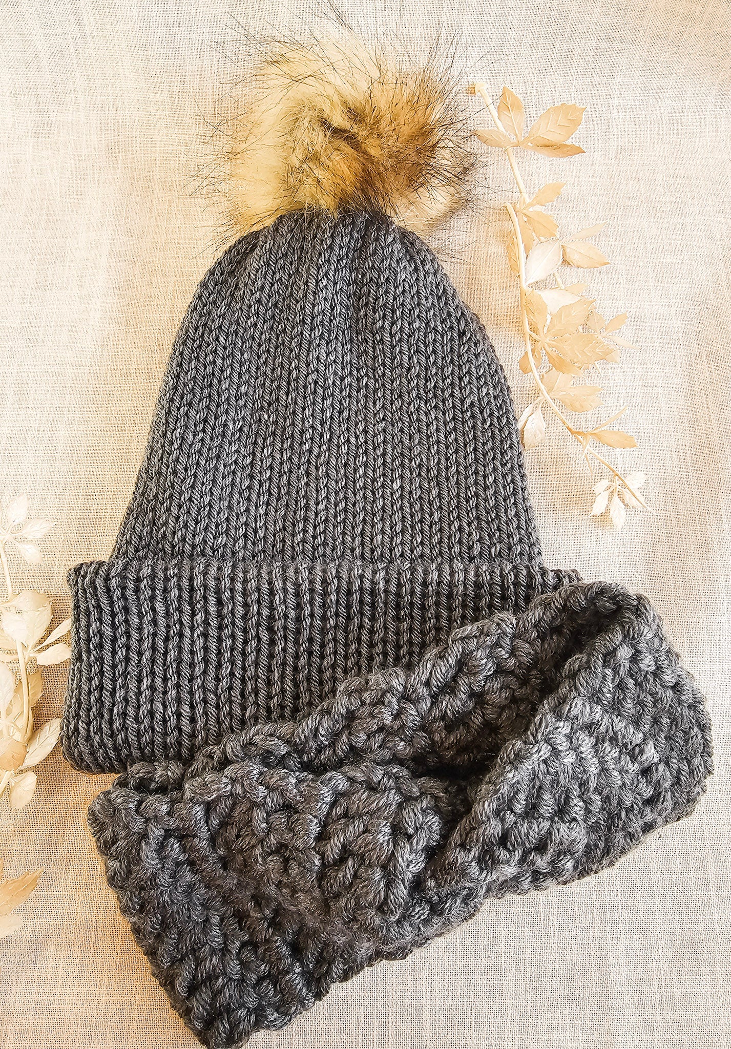 Gray knit beanie with pom-pom and matching scarf on a textured beige background