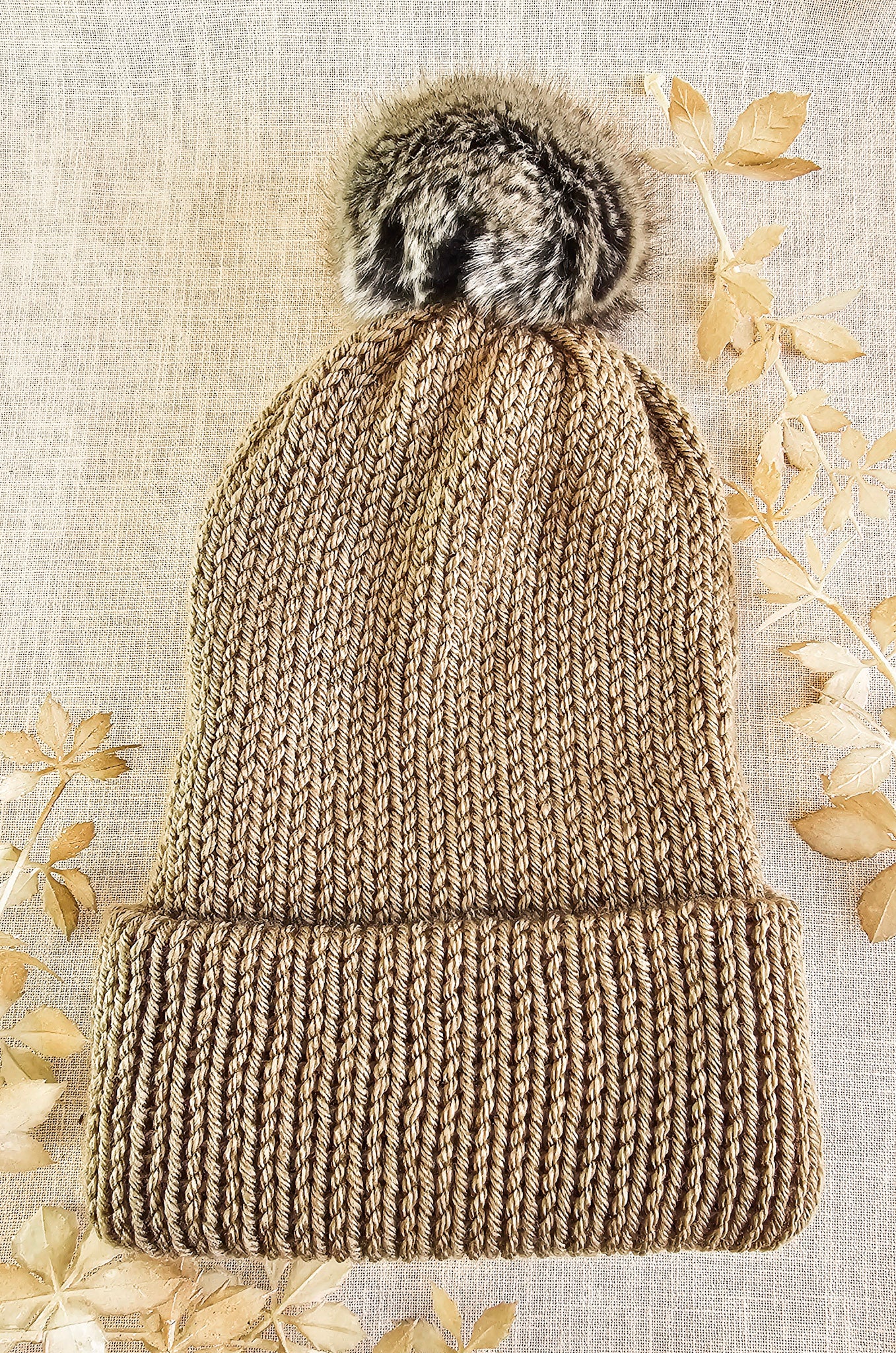 Knitted beanie with fur pom-pom on a textured beige background