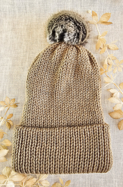 Knitted beanie with fur pom-pom on a textured beige background