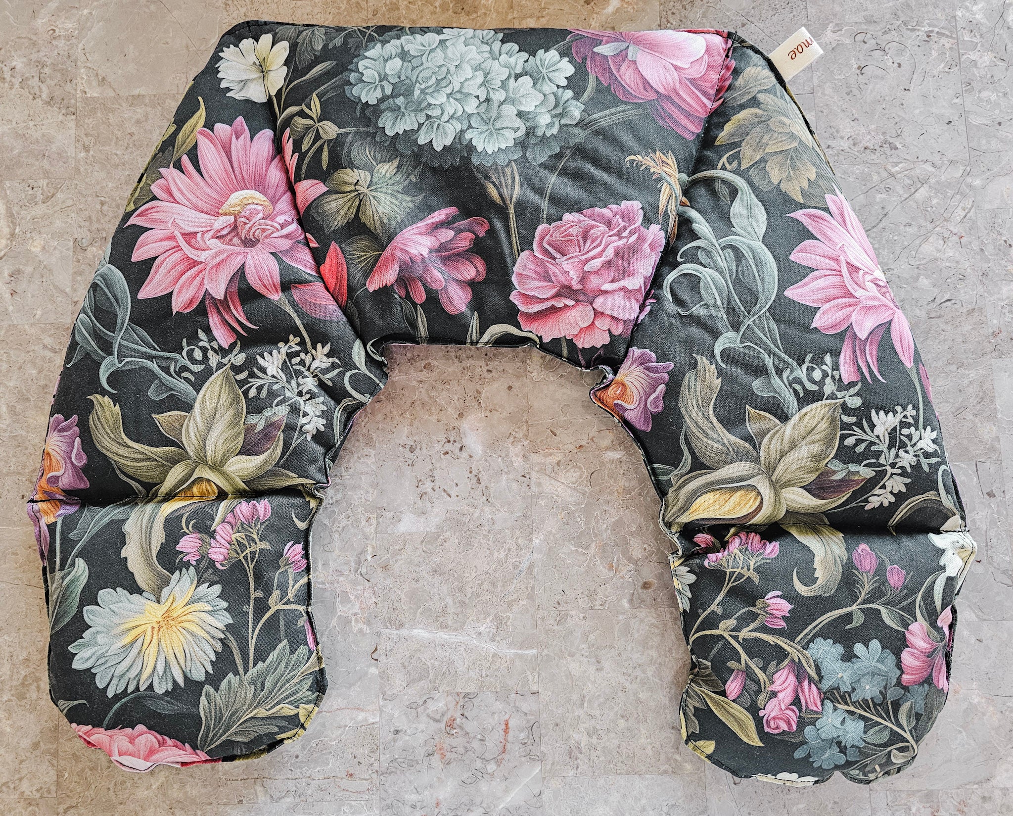 Hot and Cold Neck Pack with a dark charcoal background and a detailed floral print featuring pink, white, and green flowers, laid flat on a textured stone surface.