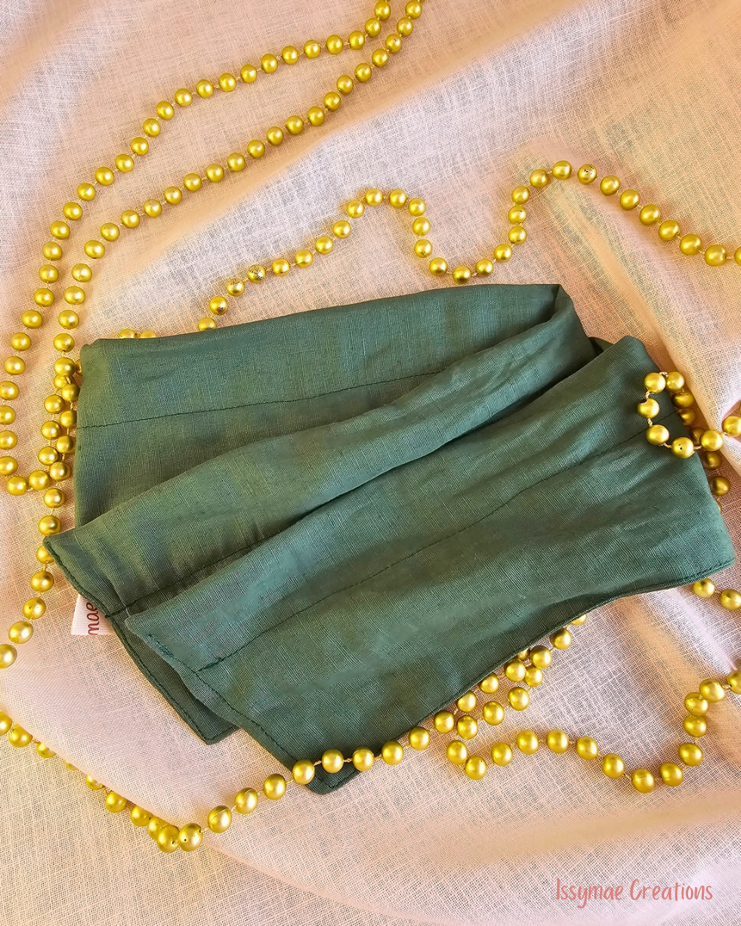 Deck the Halls forest green wire head wrap laid flat on cream fabric with gold Christmas beads.
