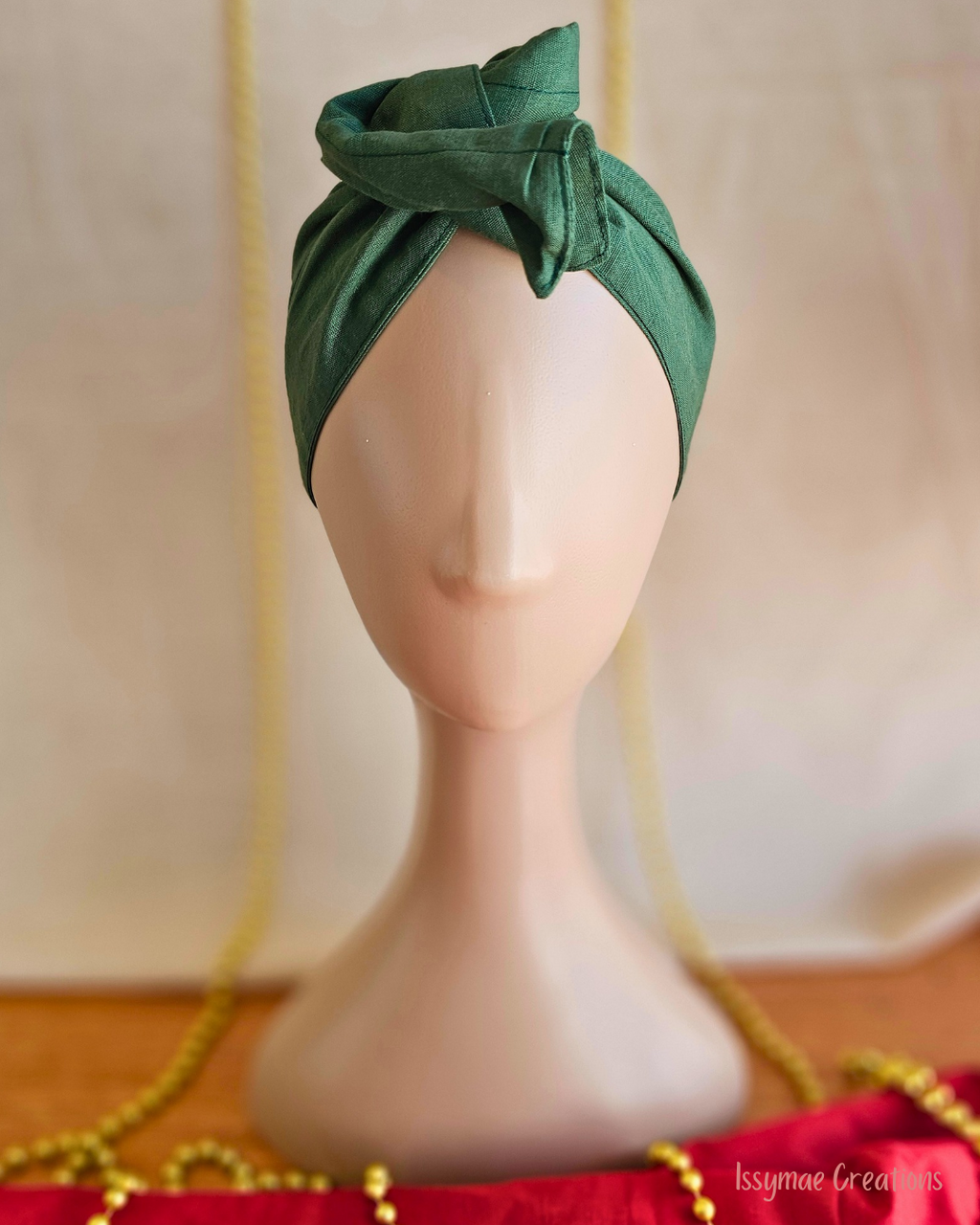 Deck the Halls forest green wire head wrap twisted into a tall rosette on a mannequin, front view.
