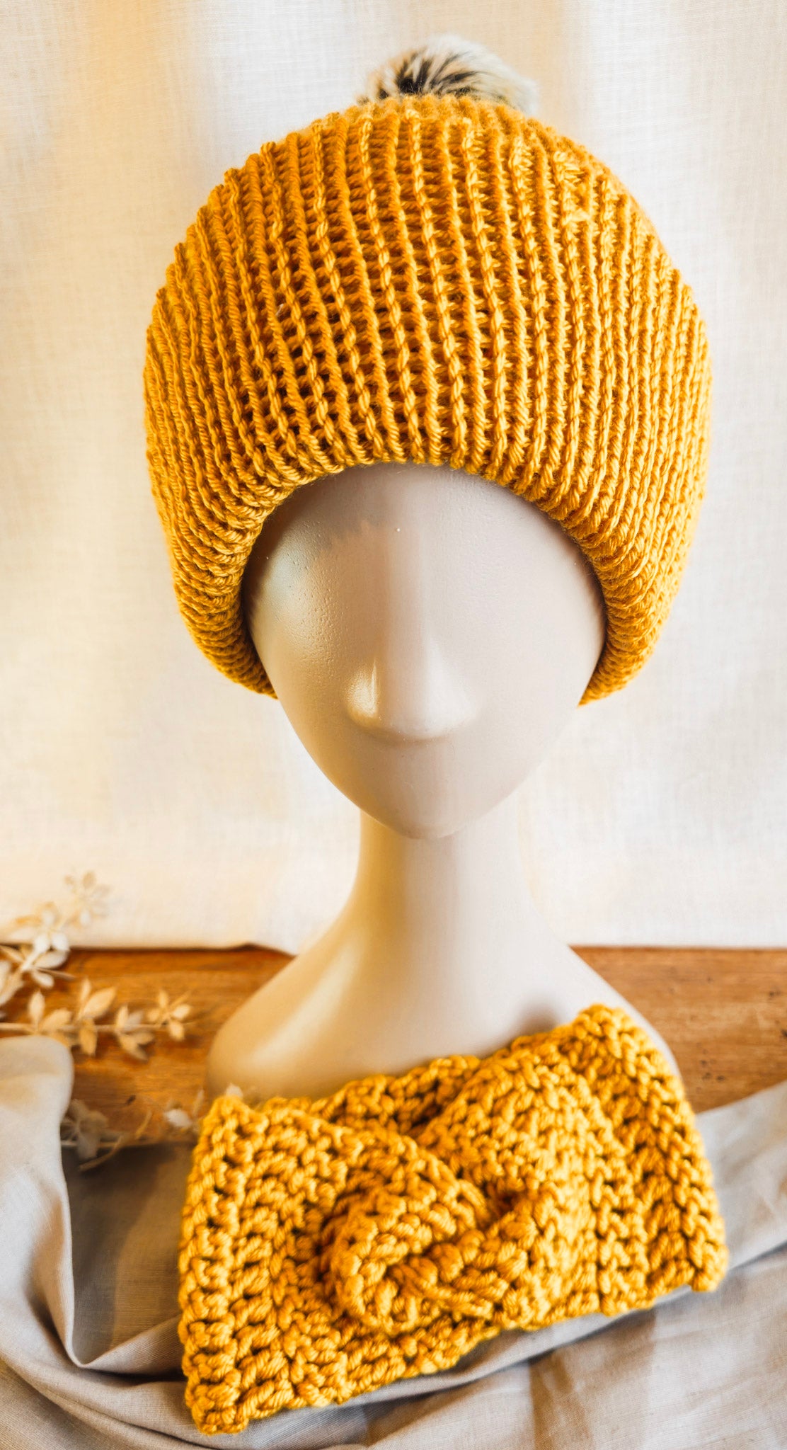 Mustard yellow knitted hat and headband on a mannequin against a neutral background