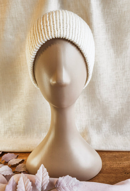 Knitted beige beanie on a mannequin head with a neutral background