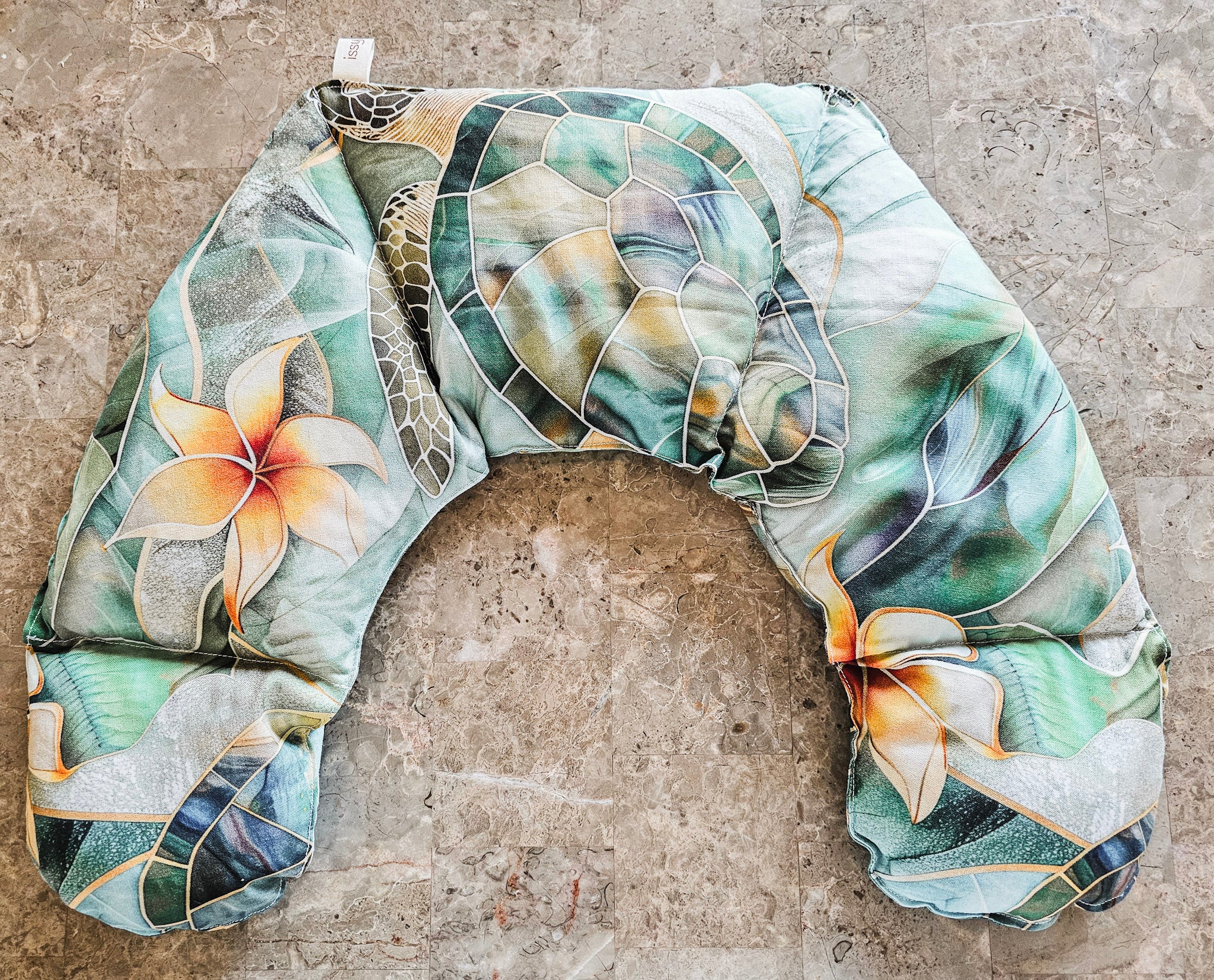 Hot and Cold neck pack with a tropical floral and leaf pattern in shades of green, beige, and orange, laid flat on a textured stone surface.
