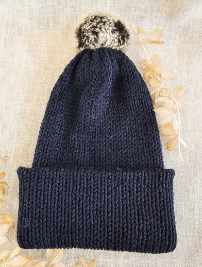 Navy blue knit beanie with a fluffy pom-pom on a textured beige background