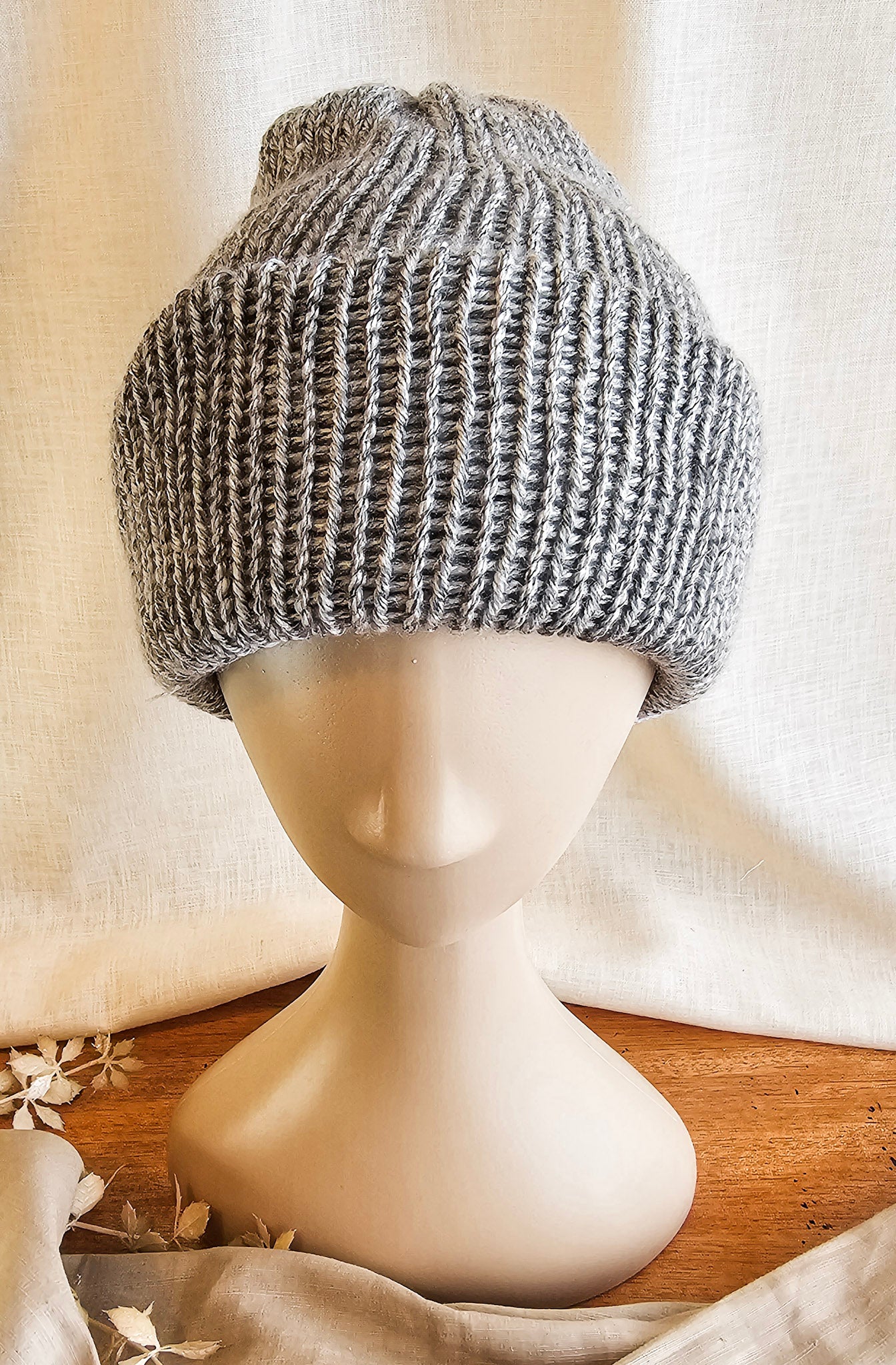 Knitted gray beanie on a mannequin head with a neutral background