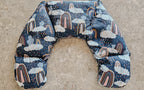 Hot and Cold Neck Pack with a navy blue background, featuring a whimsical print of white clouds, raindrops, and pastel rainbow arches, laid flat on a textured concrete surface.