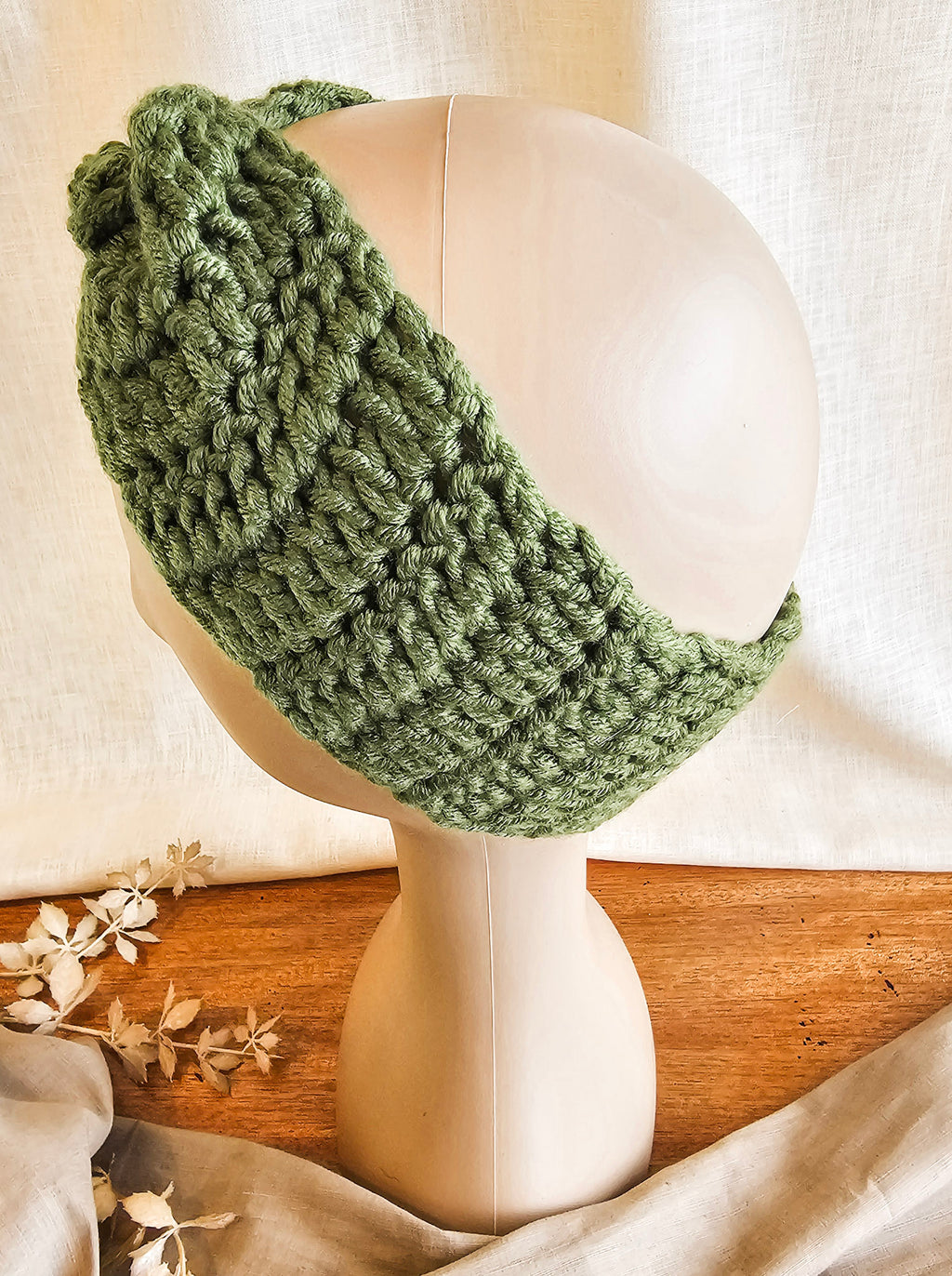 Green knitted headband on a mannequin head with a soft background