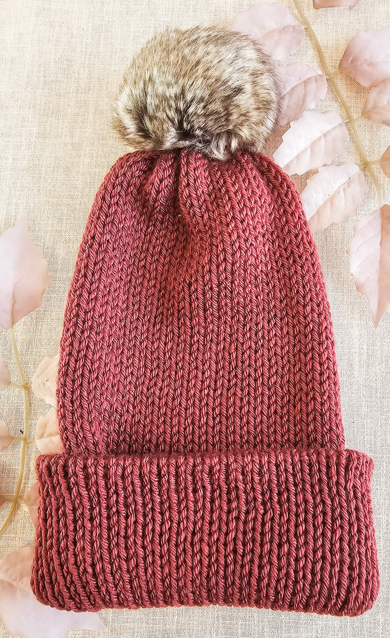 Knitted beanie with a fur pom-pom on a textured background