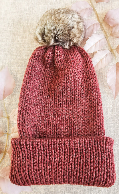 Knitted beanie with a fur pom-pom on a textured background