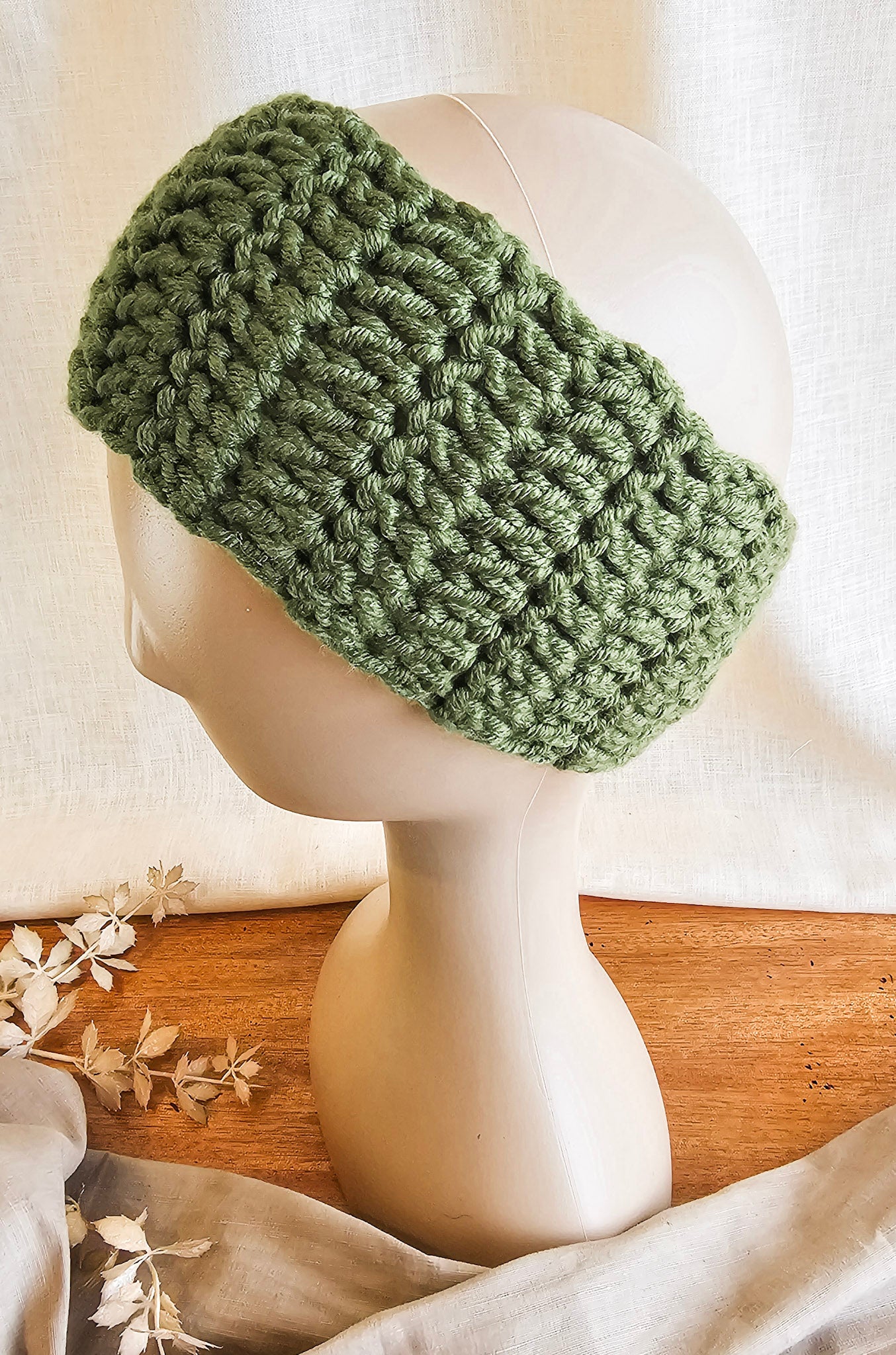 Green knitted headband on a mannequin head with a neutral background