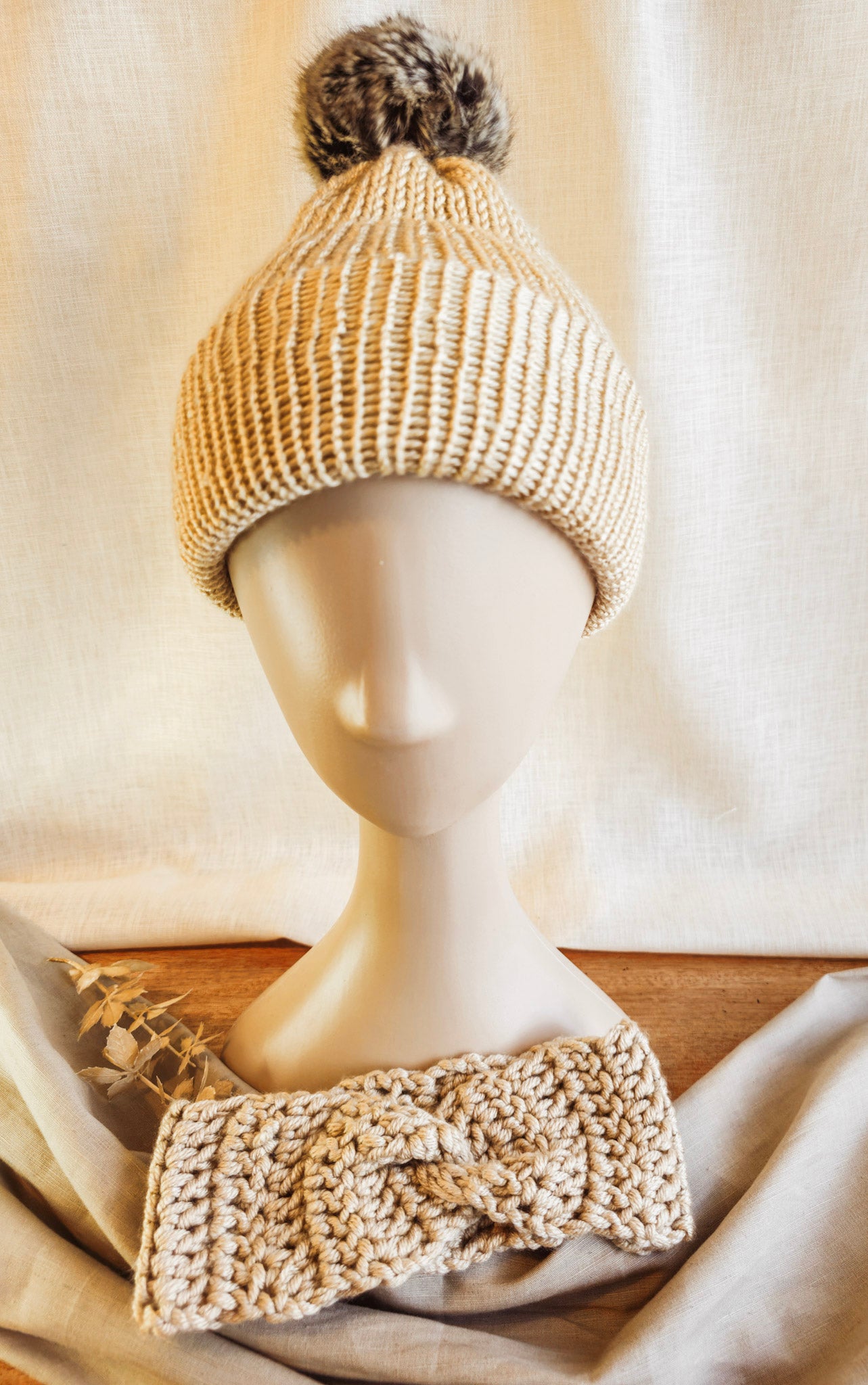 Knitted beige beanie with pom-pom on a mannequin head against a neutral background