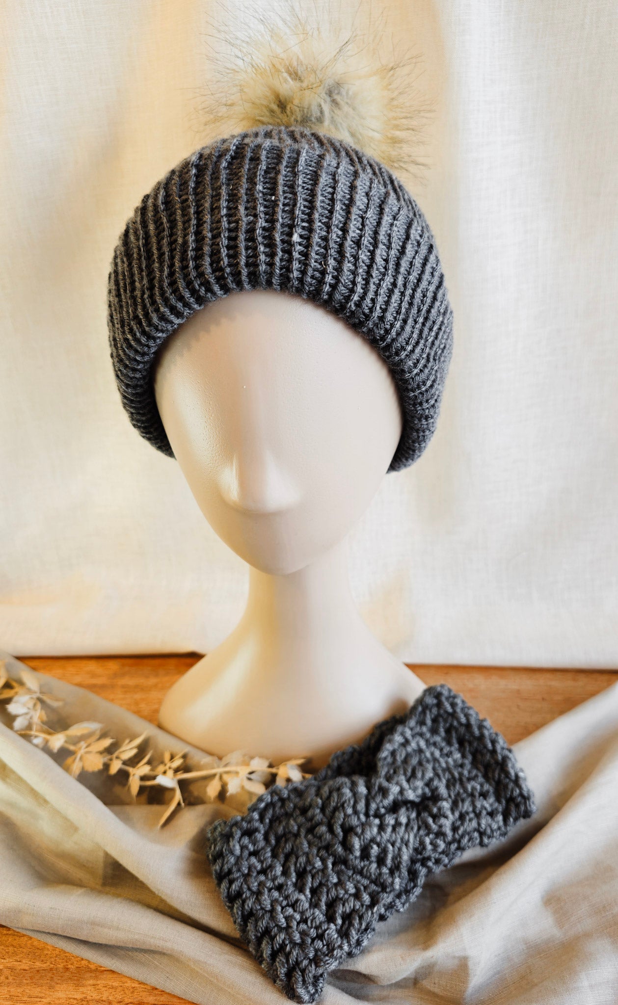 Gray knitted beanie and headband on a mannequin head with a soft white background