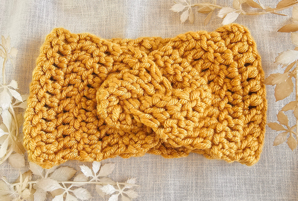 Knitted mustard yellow headband on a textured beige background with floral patterns