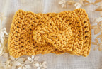 Knitted mustard yellow headband on a textured beige background with floral patterns