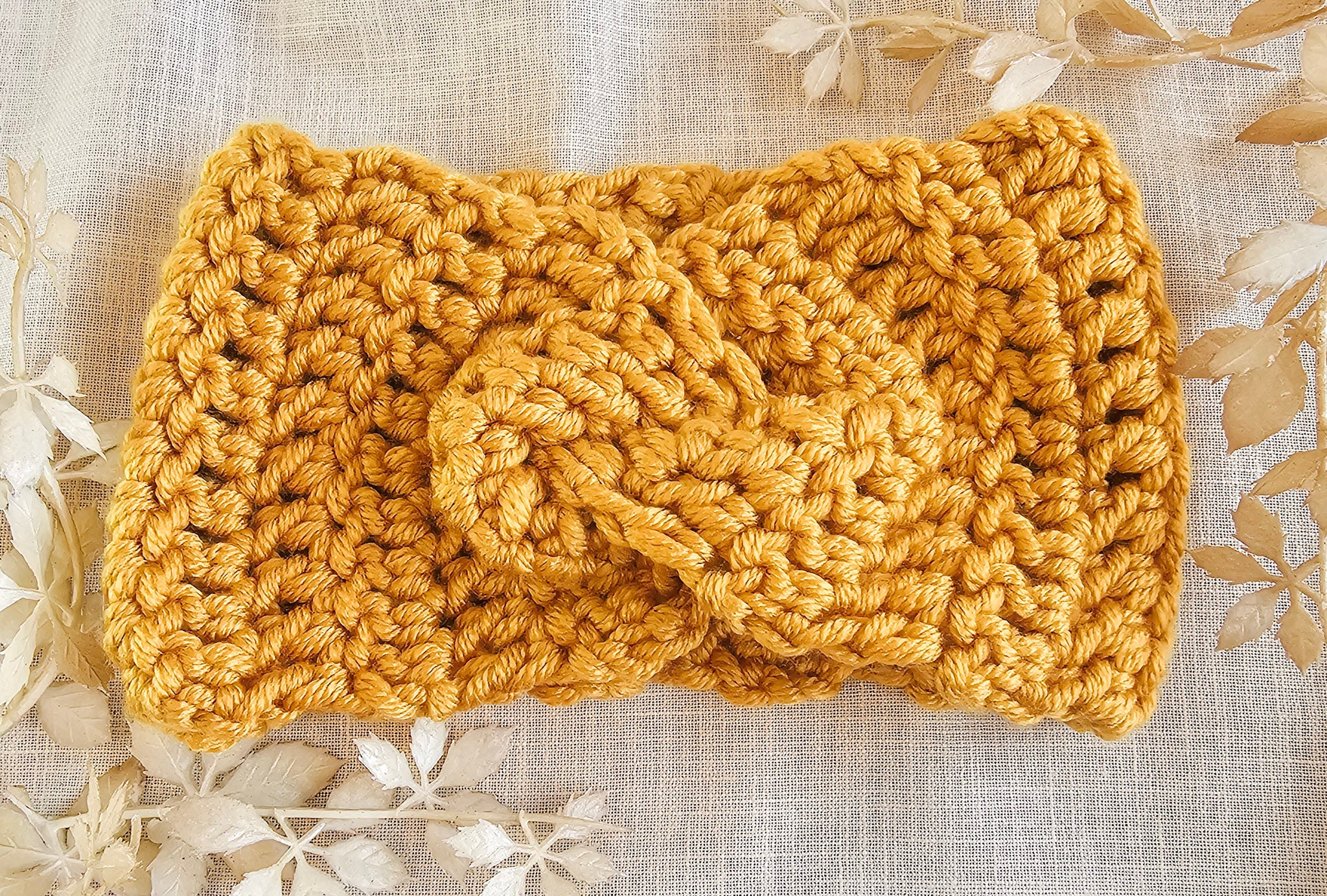 Knitted mustard yellow headband on a textured beige background with floral patterns