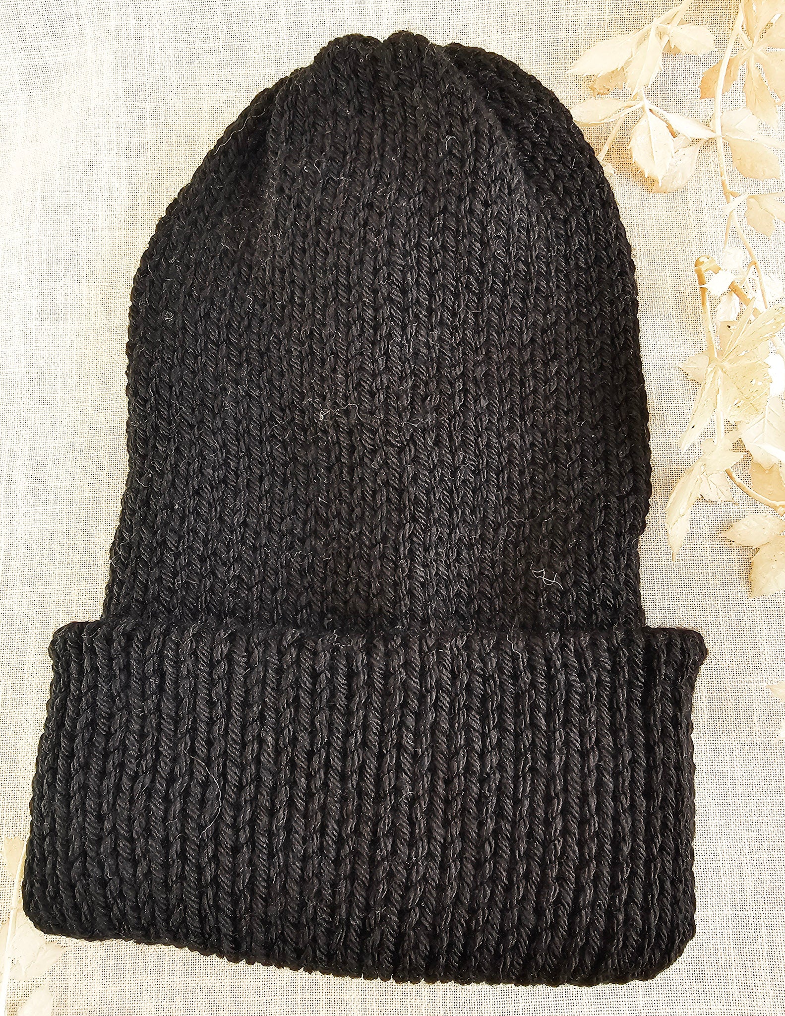 Black knit beanie on a textured beige background