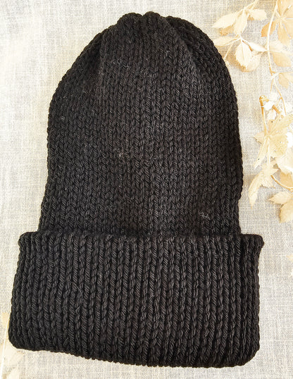 Black knit beanie on a textured beige background