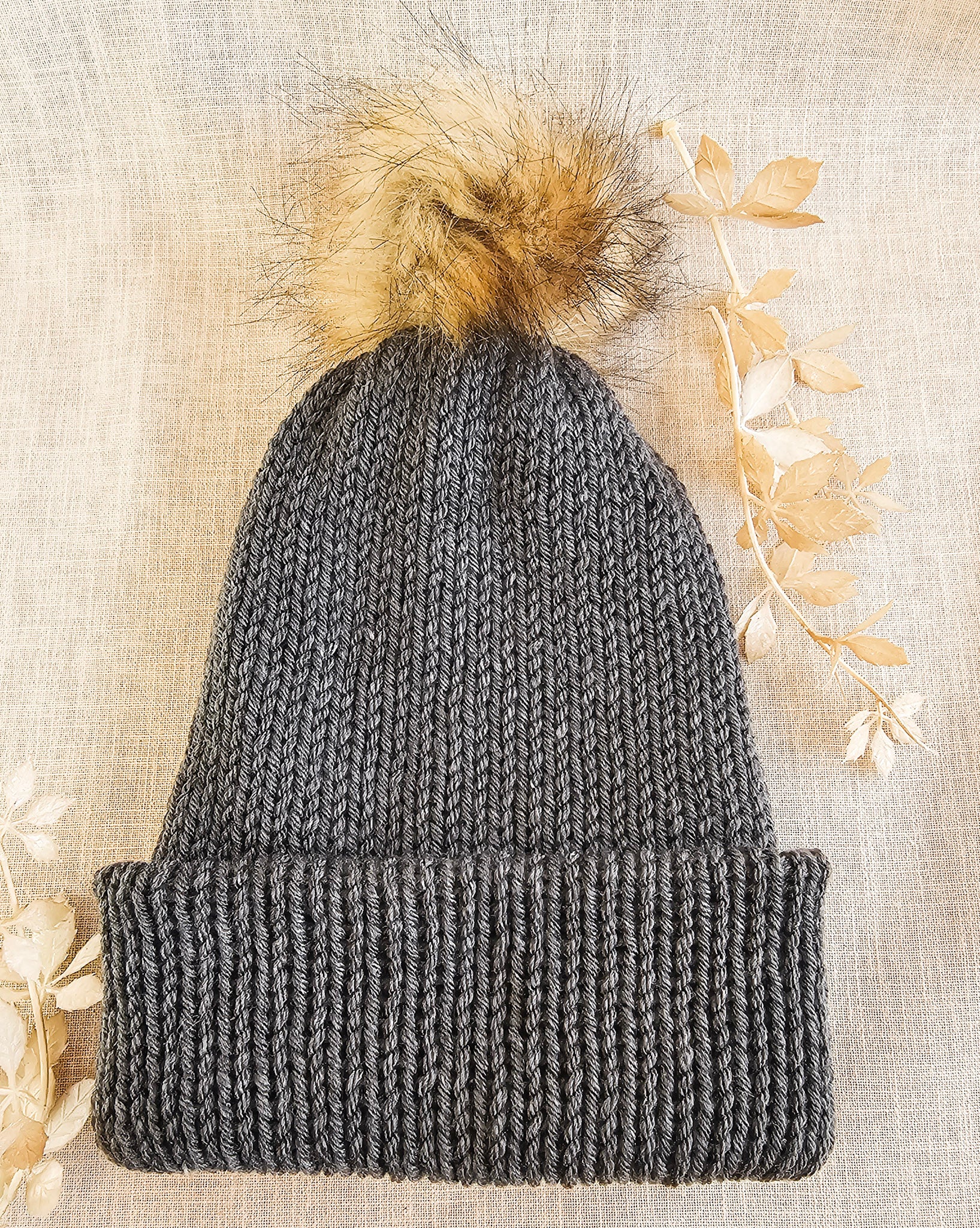 Gray knit beanie with a fur pom-pom on a textured beige background