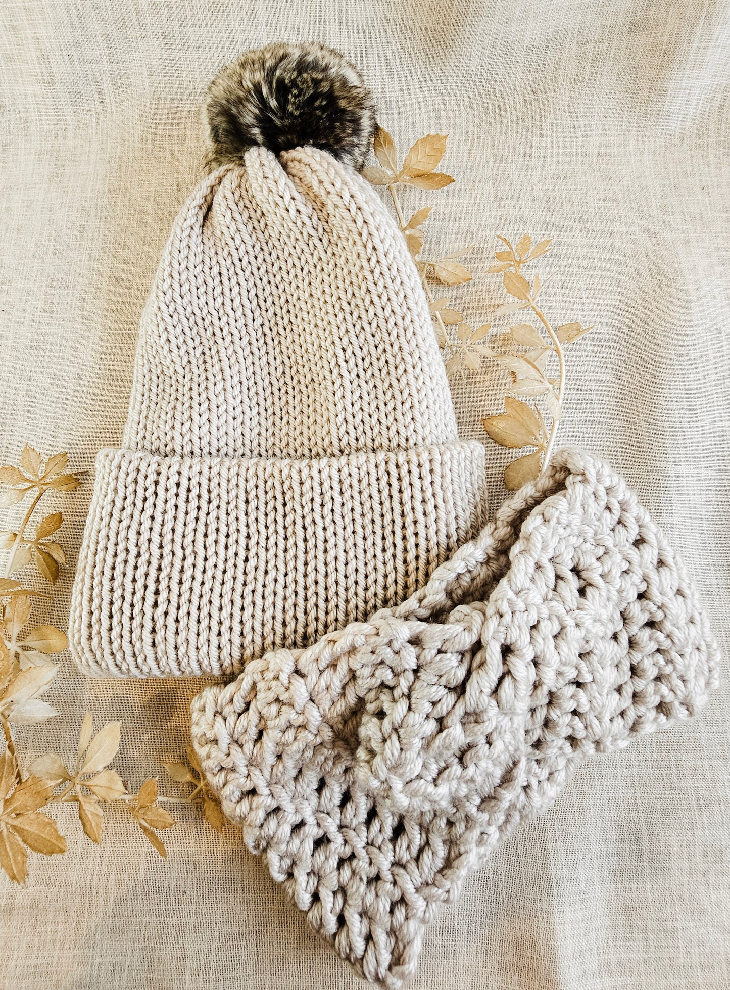 Knitted beige hat and scarf set on a textured beige background with floral patterns.