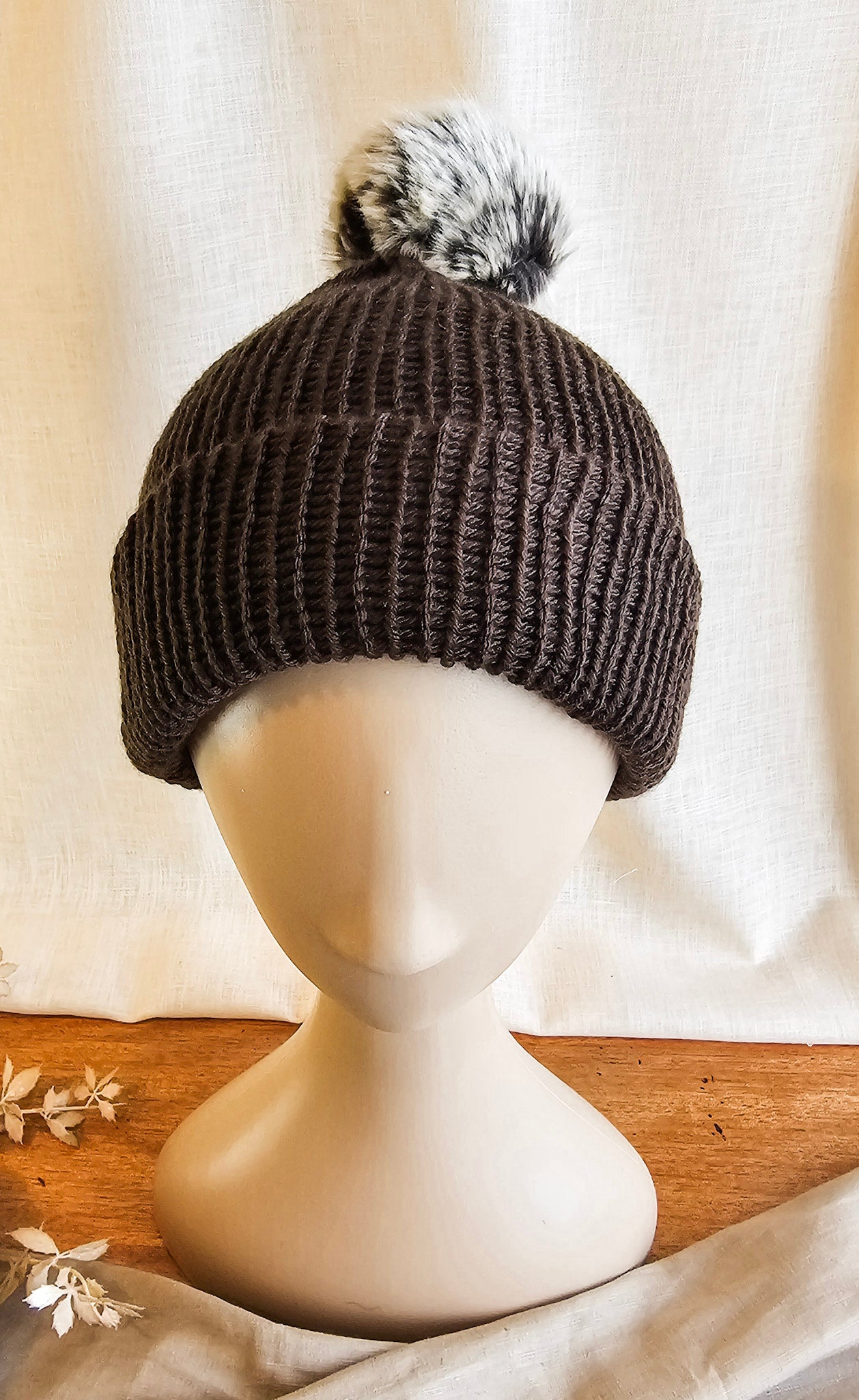 Brown knit beanie with a pom-pom on a mannequin head against a neutral background