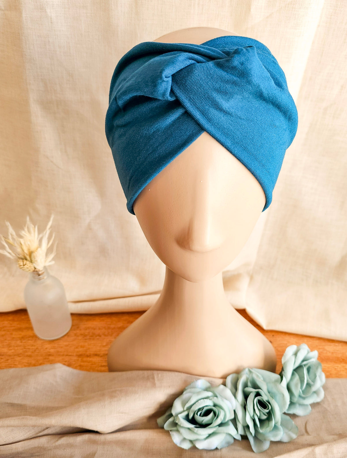 Top view of Teal knotted headband on with mannequin head with soft linen back ground