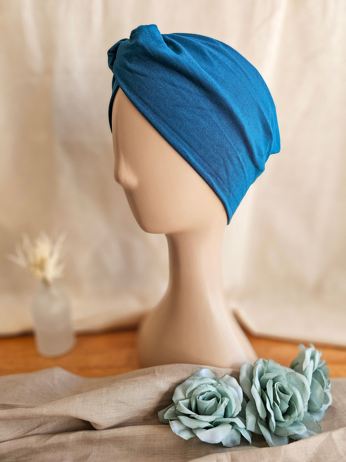 side view of a woman's knotted headband on white head mannequin with soft linen background
