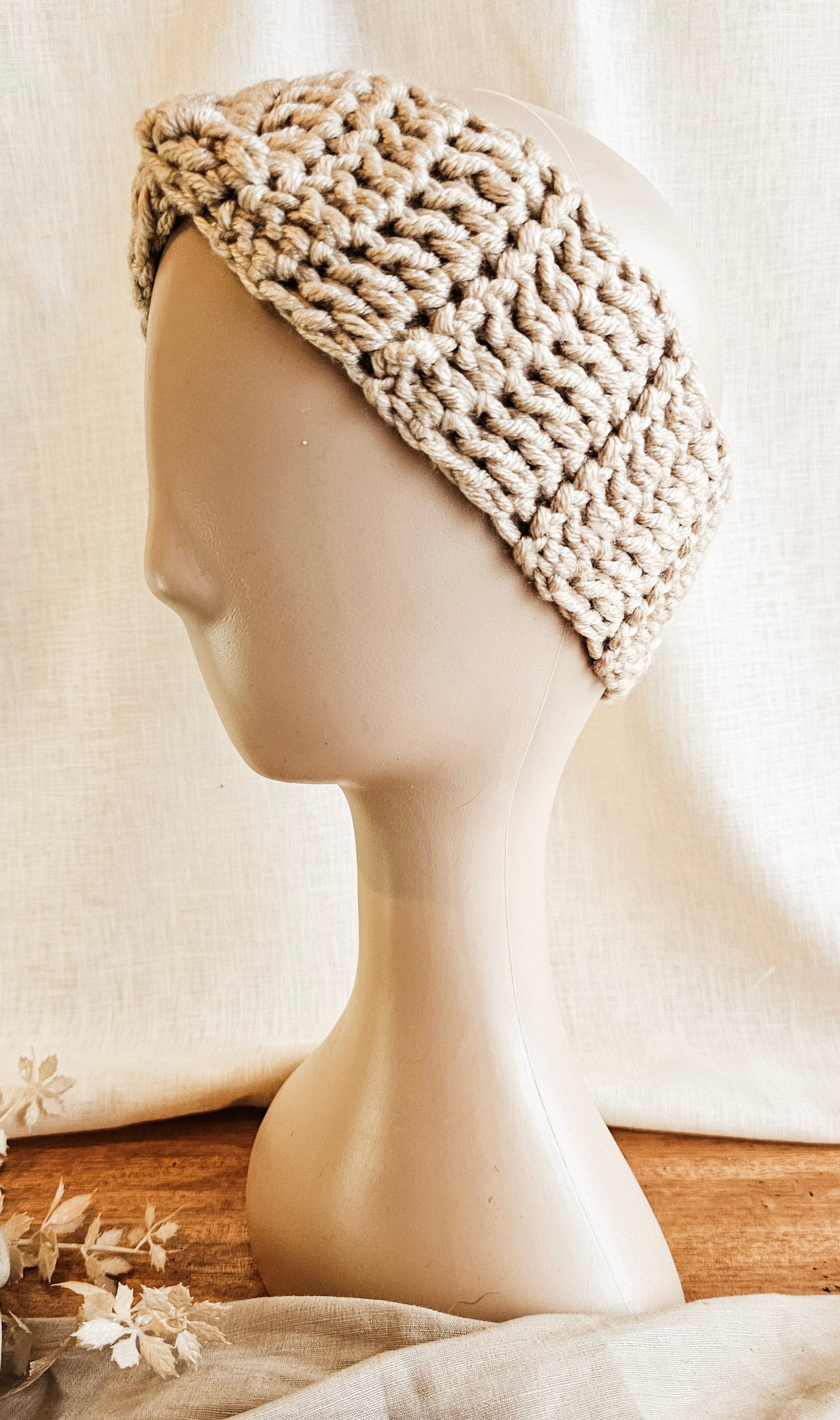 Beige knitted headband on a mannequin head with a neutral background