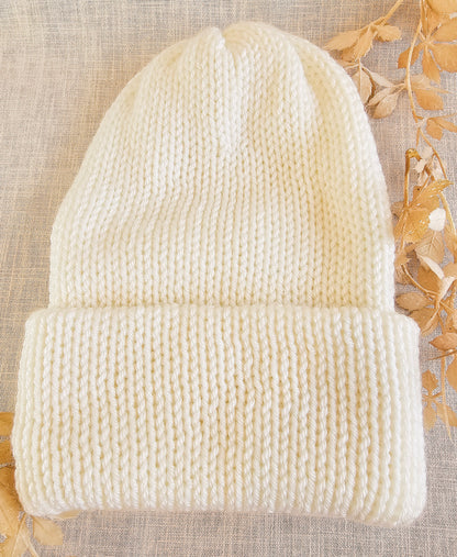Knitted cream beanie on a textured beige background with dried leaves.