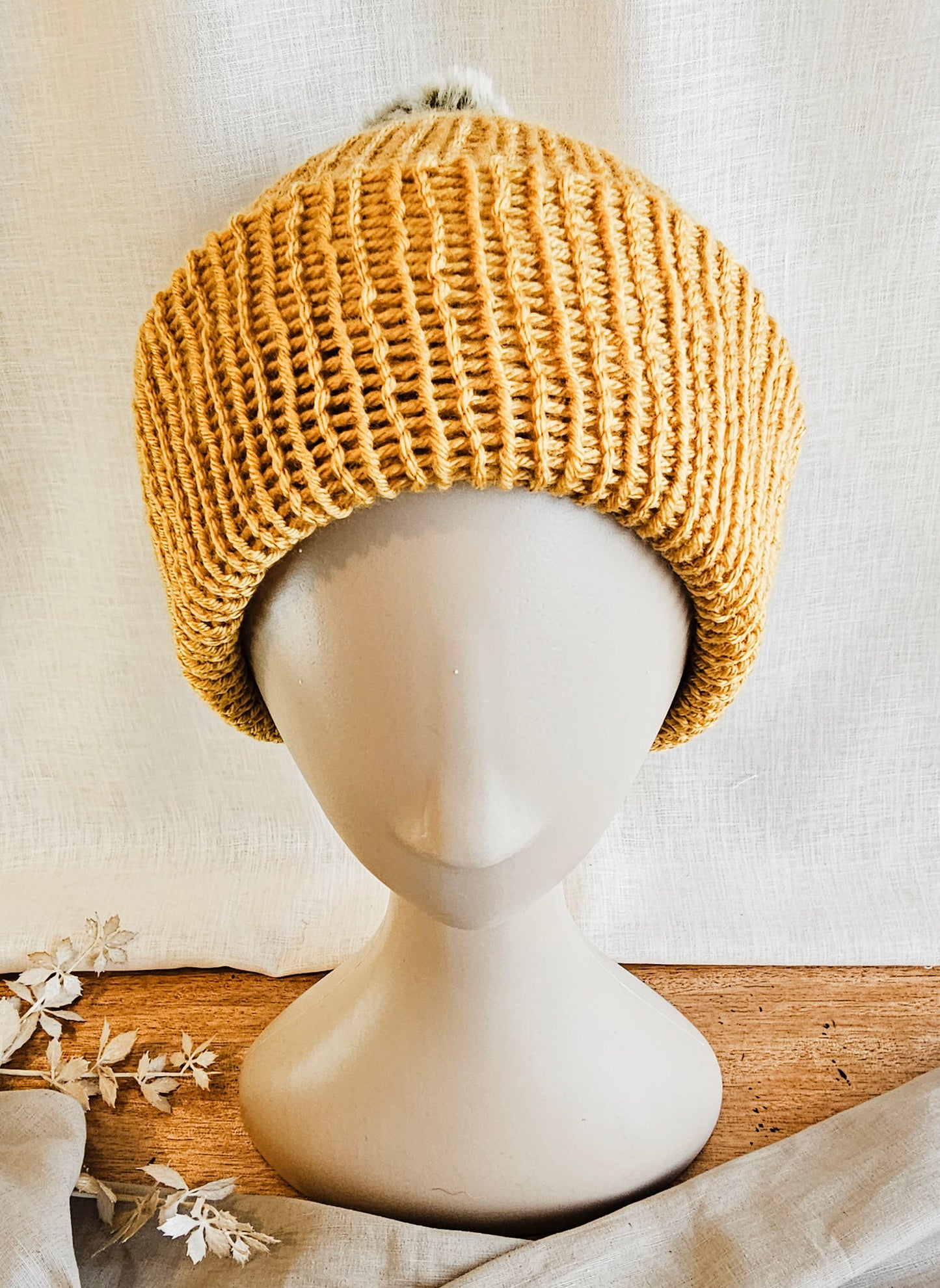 Knitted beige beanie on a mannequin head against a neutral background