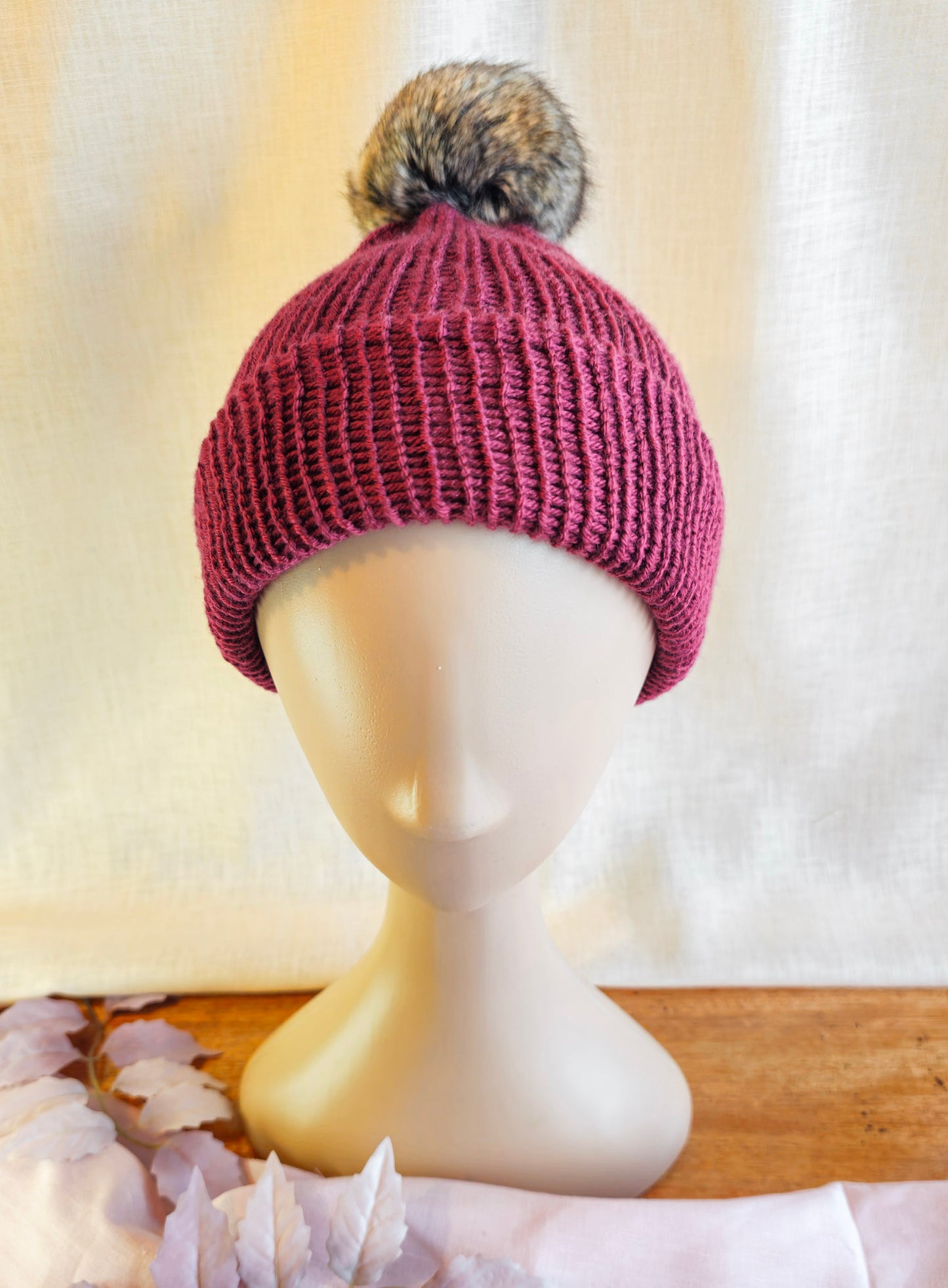 Knitted beanie with a pom-pom on a mannequin head against a neutral background