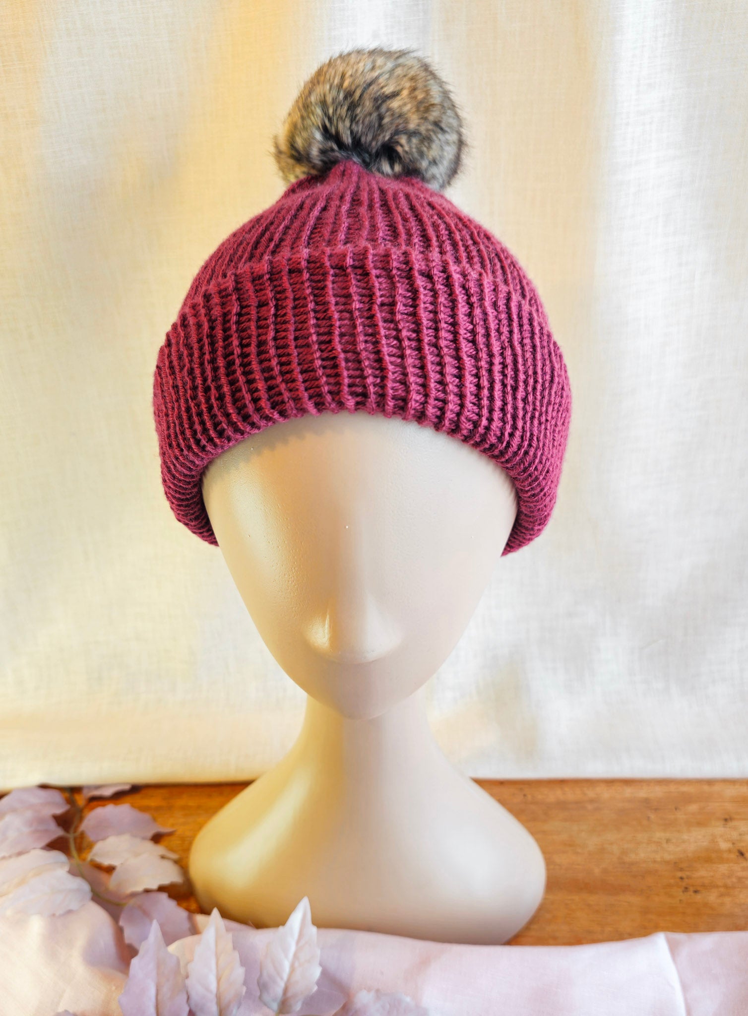 Knitted beanie with a pom-pom on a mannequin head against a neutral background