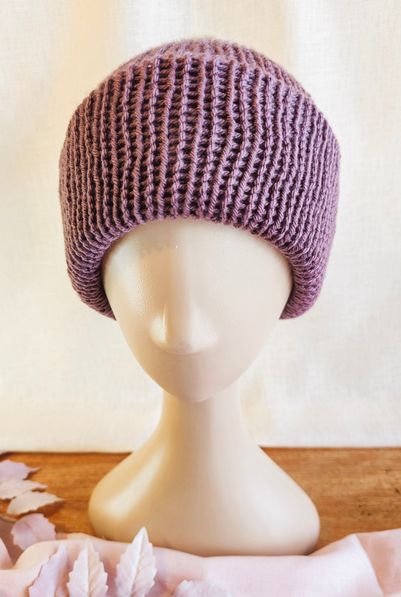Knitted purple beanie on a mannequin head with a neutral background