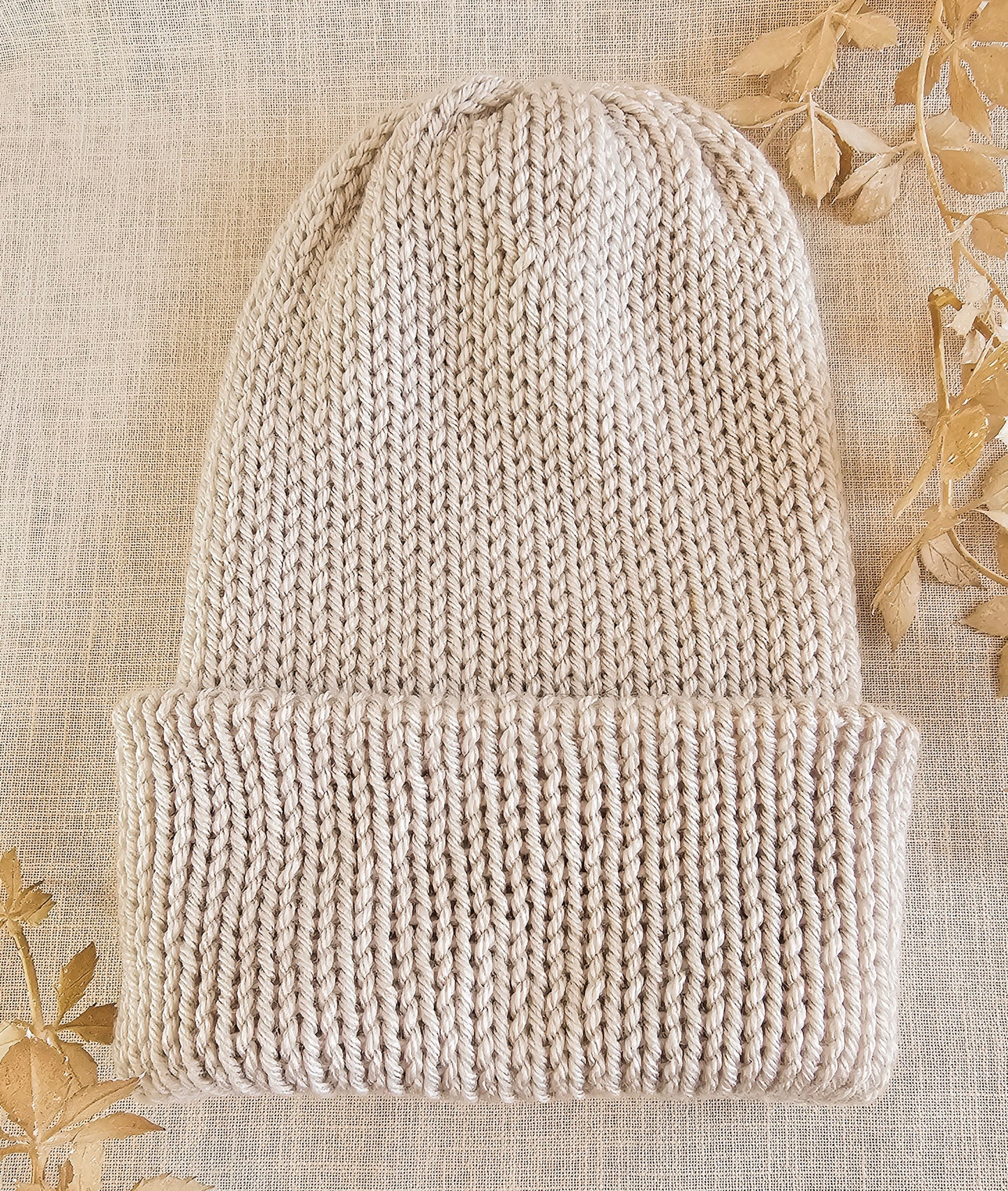 Knitted beige beanie on a textured beige background with floral patterns