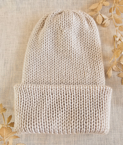 Knitted beige beanie on a textured beige background with floral patterns