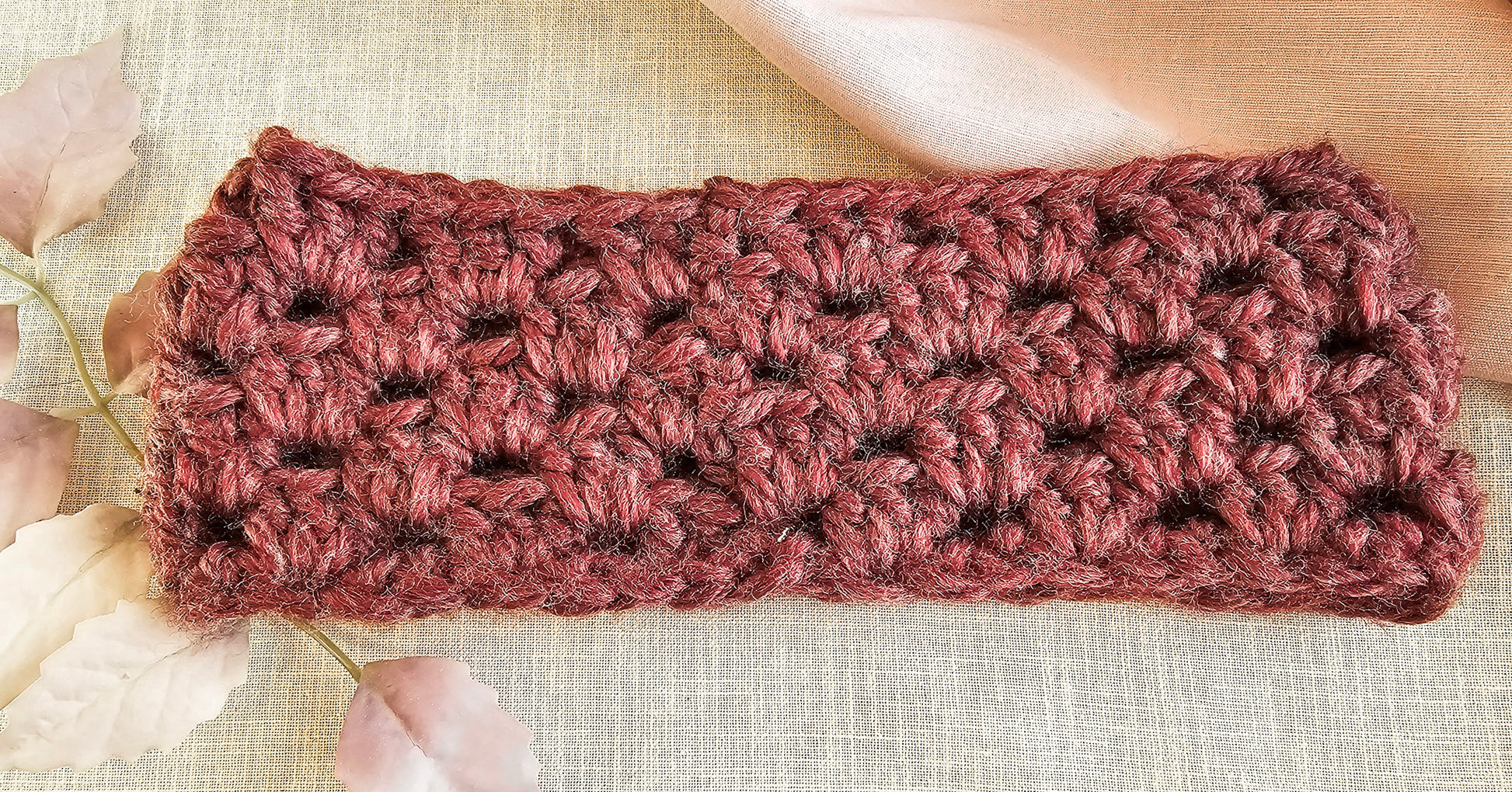 Crocheted headband in pinkish-brown on a textured beige background