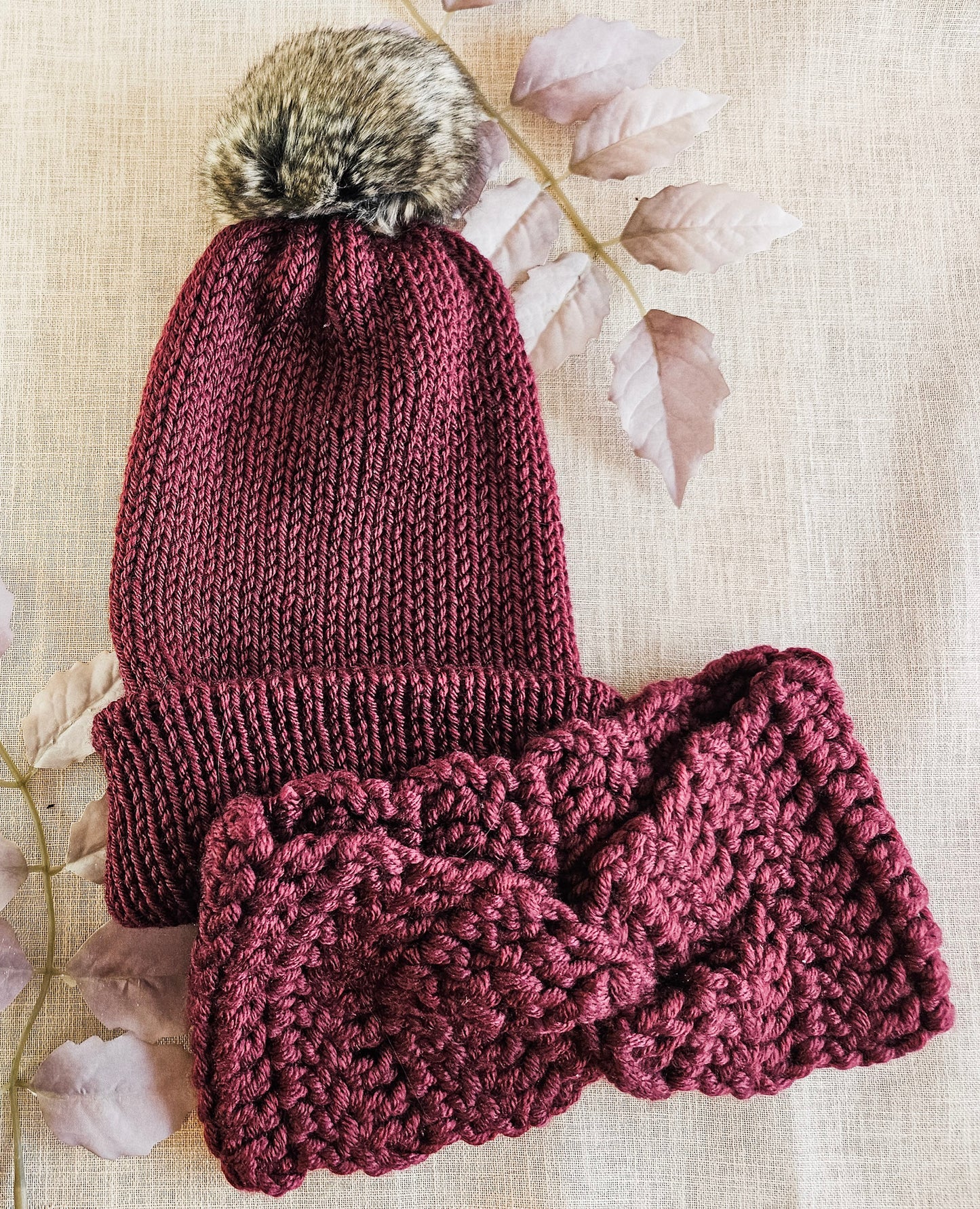 Knitted maroon hat and scarf set with fur pom-pom on a light background