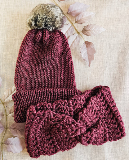 Knitted maroon hat and scarf set with fur pom-pom on a light background