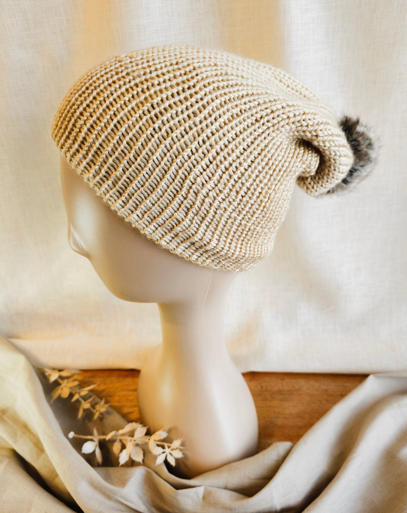 Knitted beige beanie on a mannequin head with a soft white background