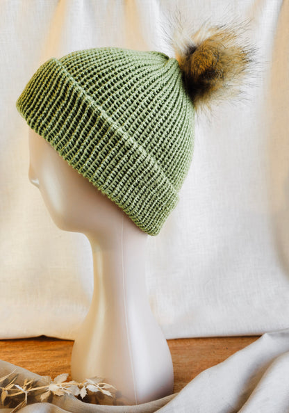 Green knitted beanie with a pom-pom on a mannequin head against a white background