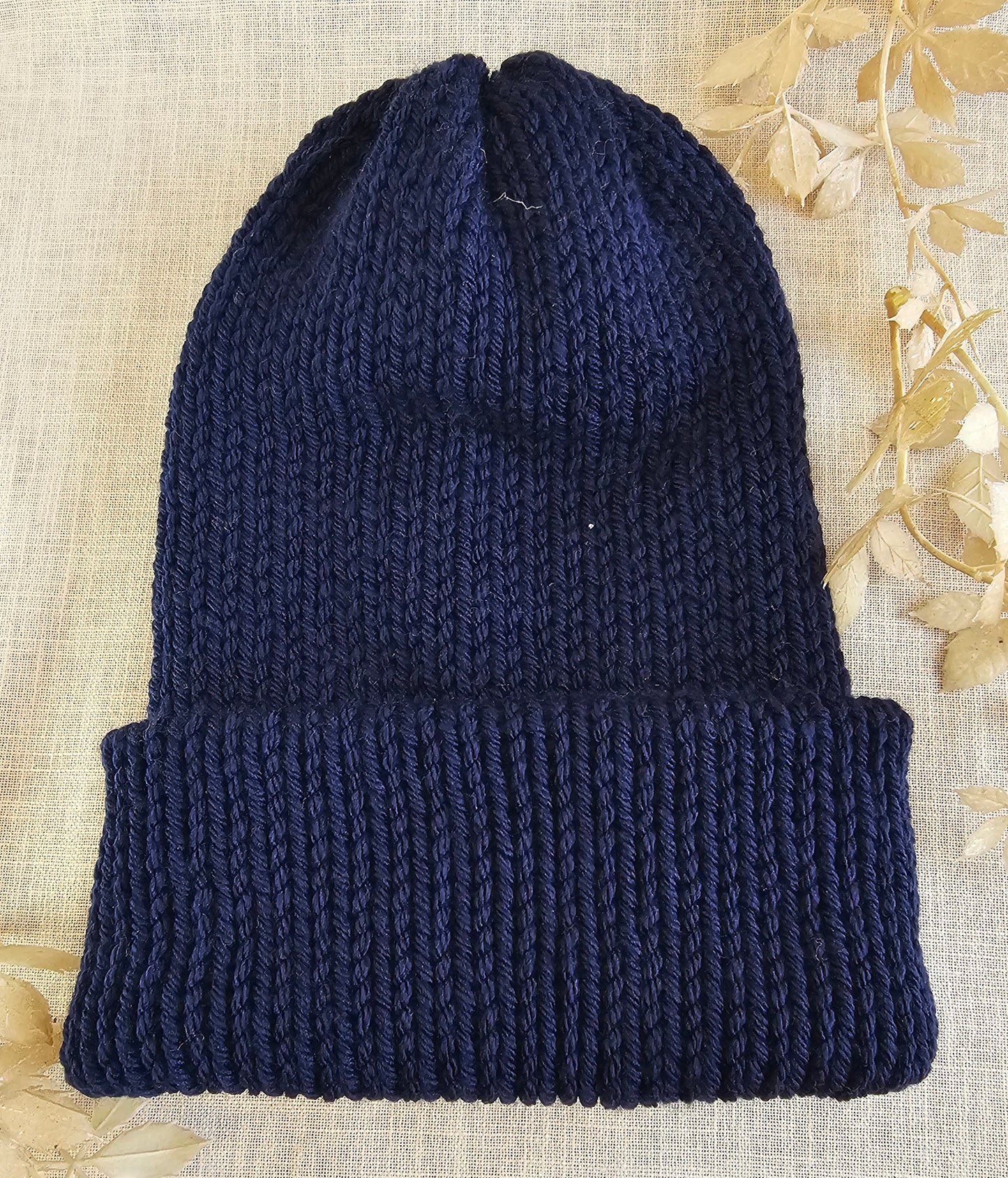 Navy blue knitted beanie on a textured beige background with dried leaves.