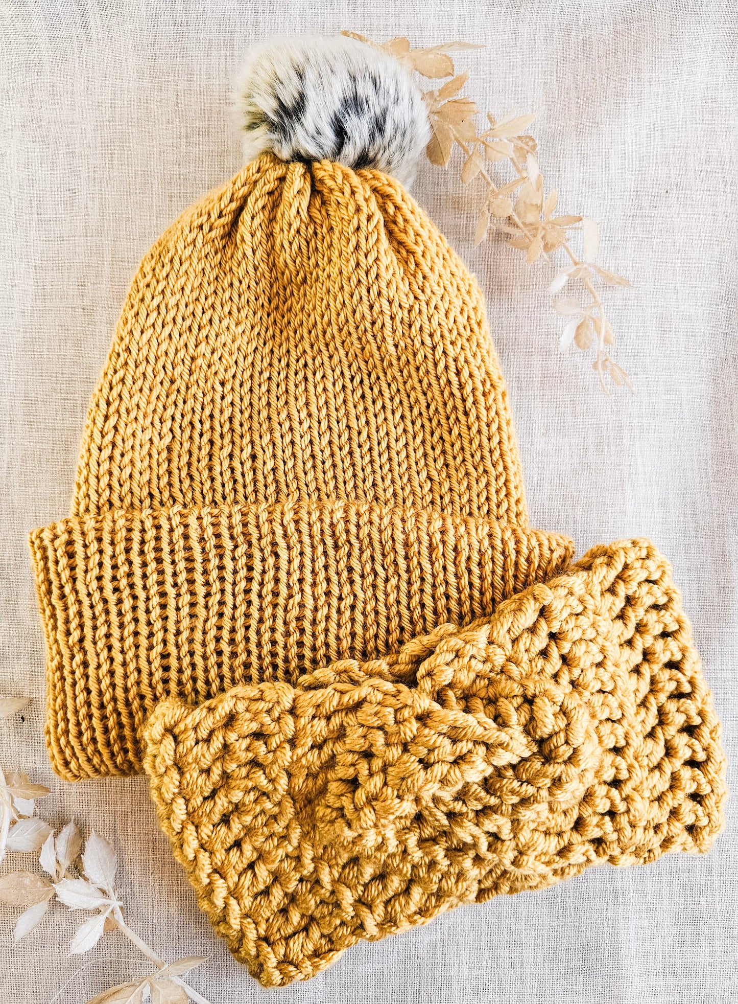 Knitted mustard yellow beanie and scarf set on a textured beige background
