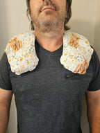 A man wearing a dark gray t-shirt with a floral-patterned neck hot and cold pack resting on his shoulders, photographed against a plain beige wall.