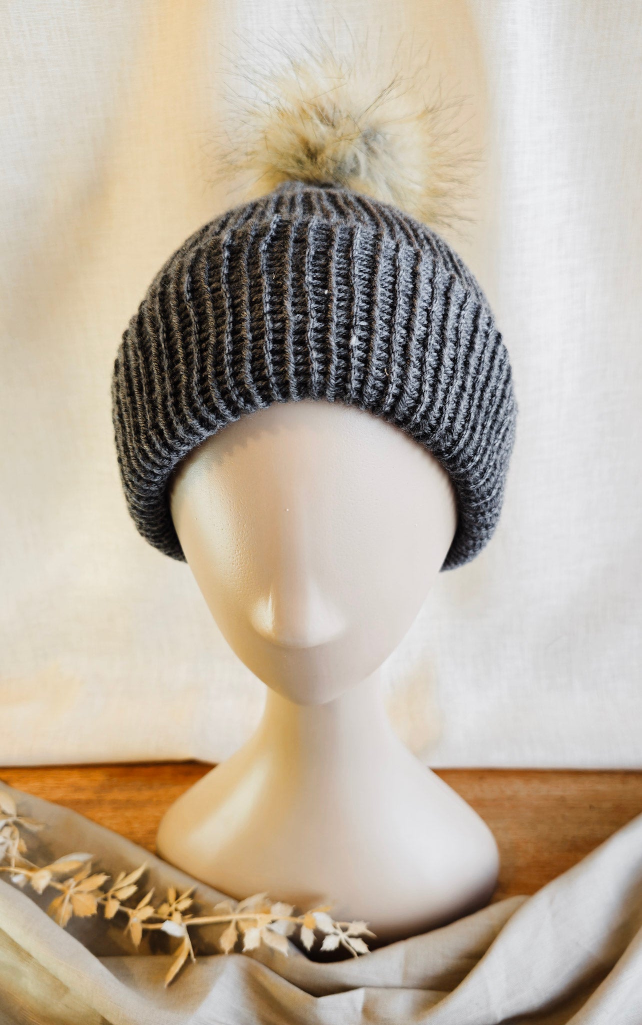 Knitted beanie with a pom-pom on a mannequin head against a neutral background