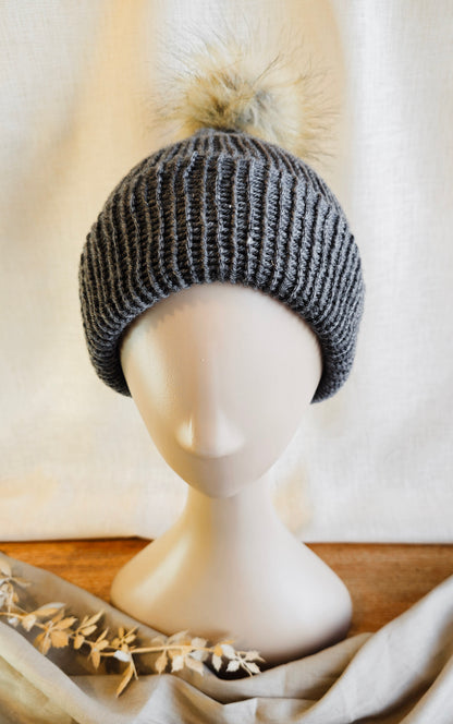 Knitted beanie with a pom-pom on a mannequin head against a neutral background