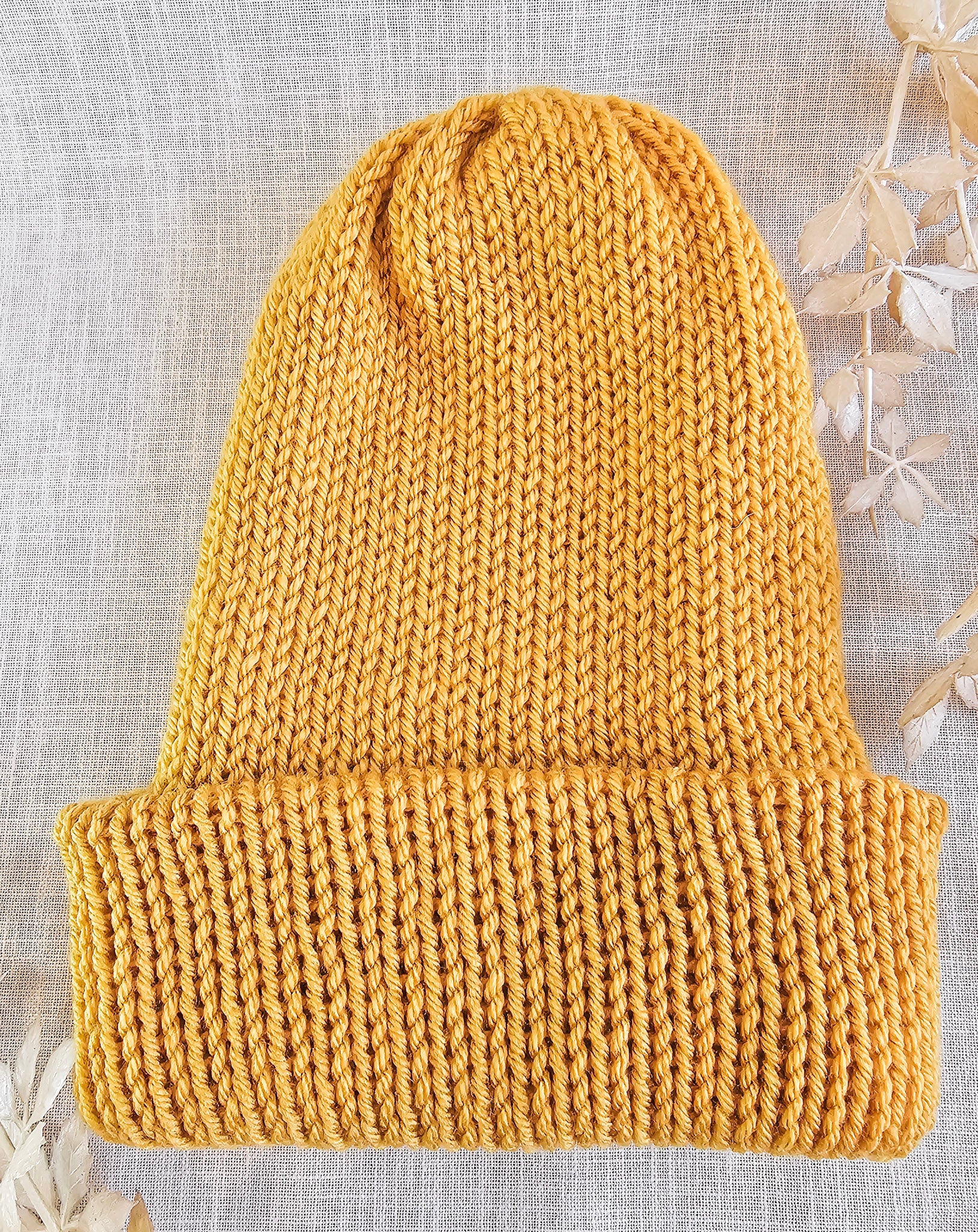 Knitted mustard yellow beanie on a textured light gray background